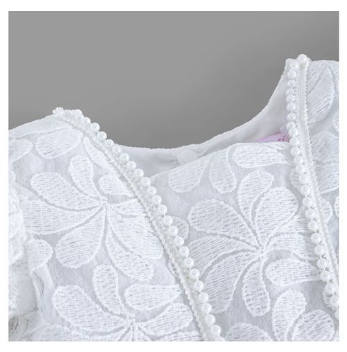 Close-up detail of white lace dress showing pearl button embellishments and floral pattern.