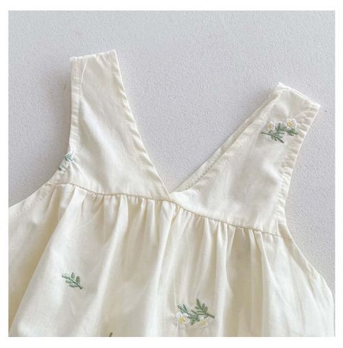 Close-up of shoulder straps with delicate floral embroidery on cream baby romper.