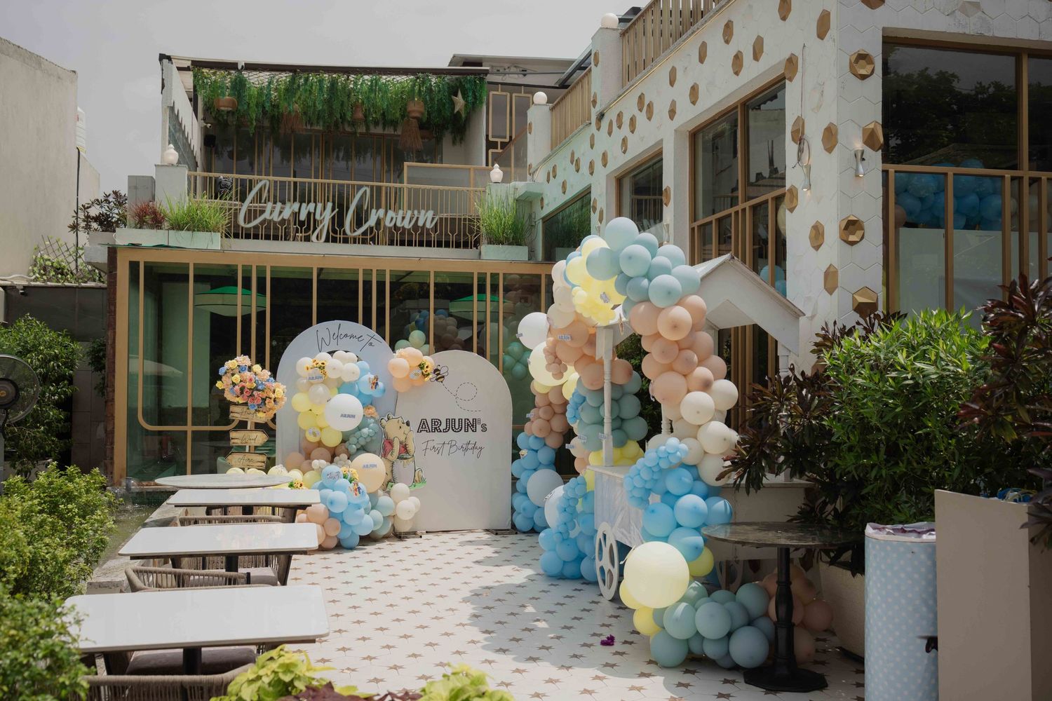 Colorful balloon arch with blue, yellow, and white balloons decorating an outdoor party venue with a Curry Crown sign.