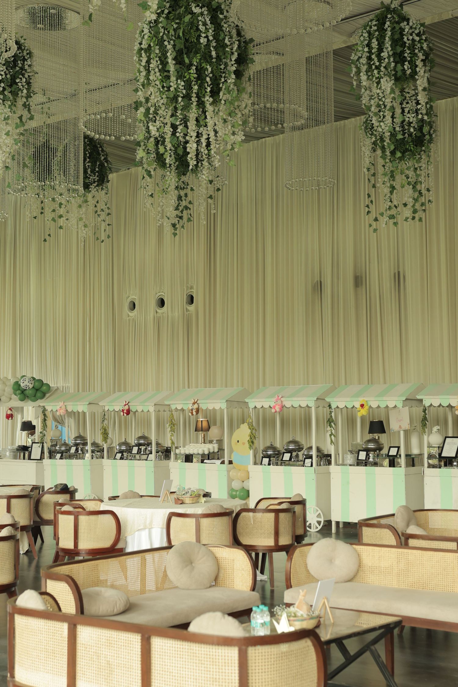 Elegant cafe interior with rattan chairs, green striped booths, hanging plants, and flowing curtains.