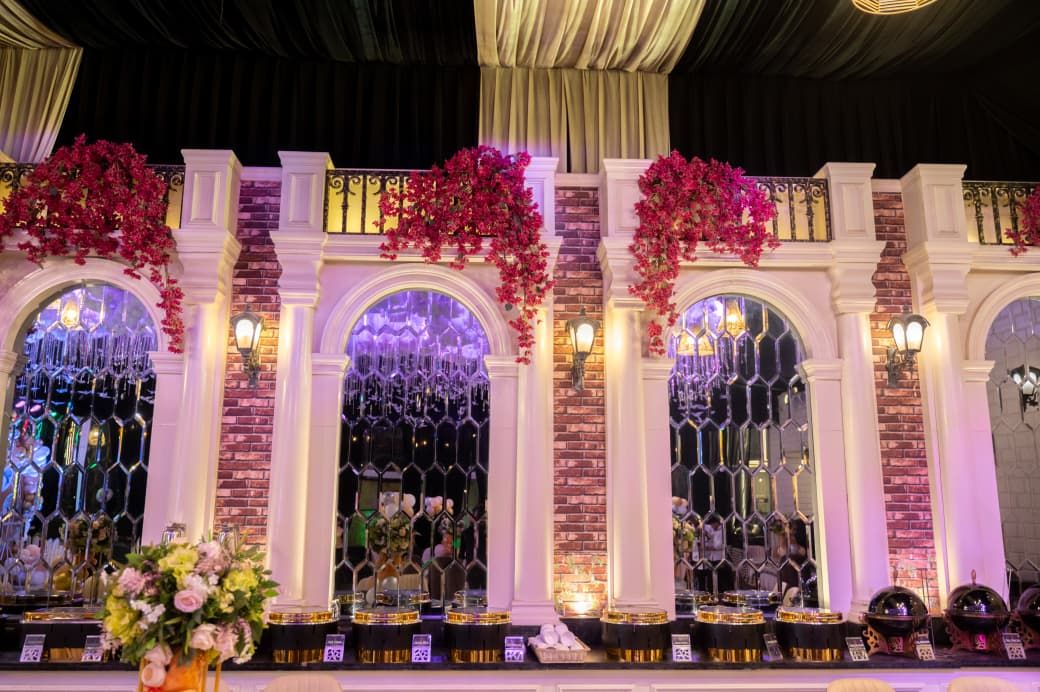 Elegant wedding reception backdrop with white arches, red brick, hanging floral arrangements, and mirrored panels with warm lighting.