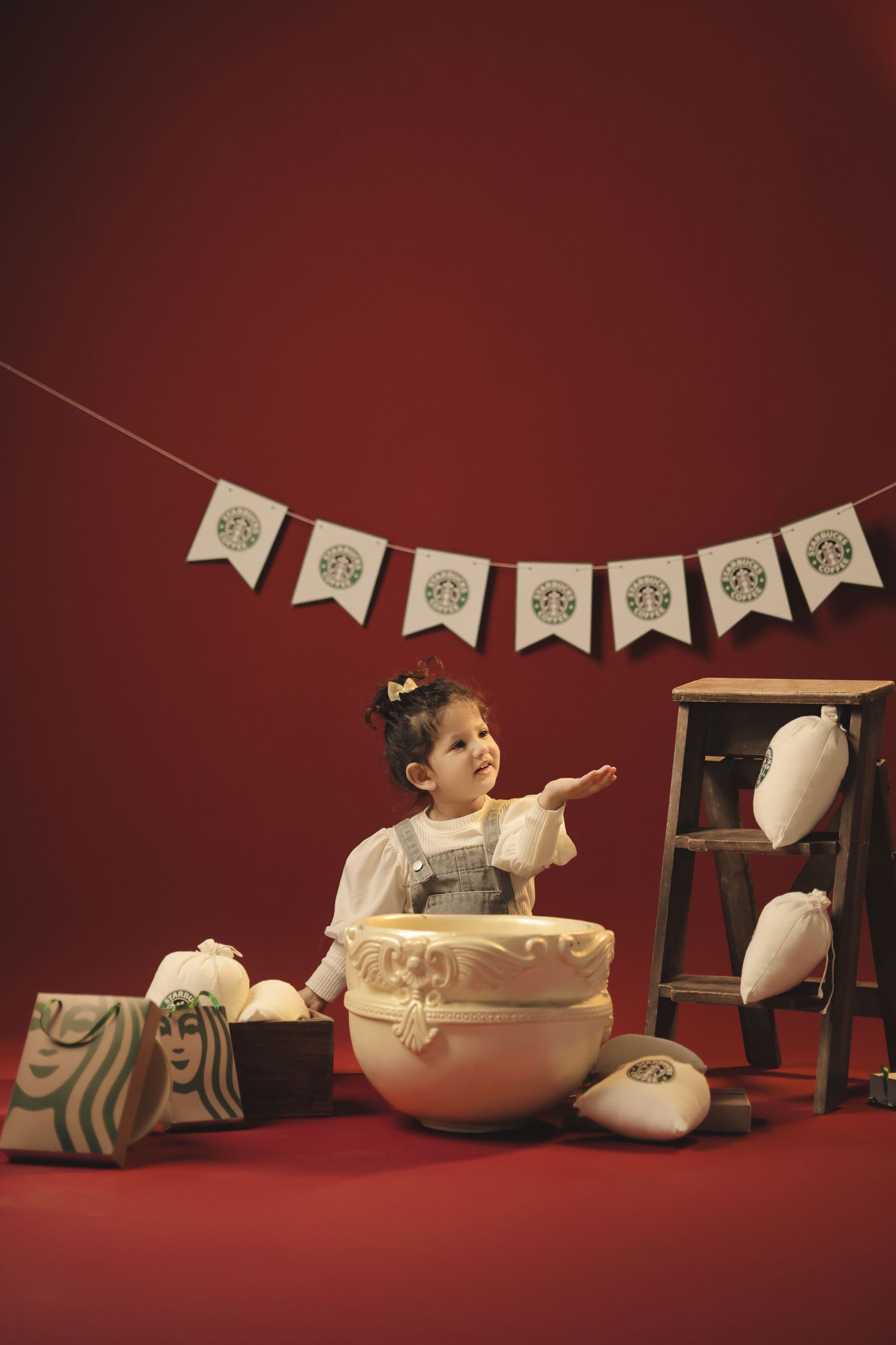 Young girl sits surrounded by Starbucks-themed props and bunting on a red background.