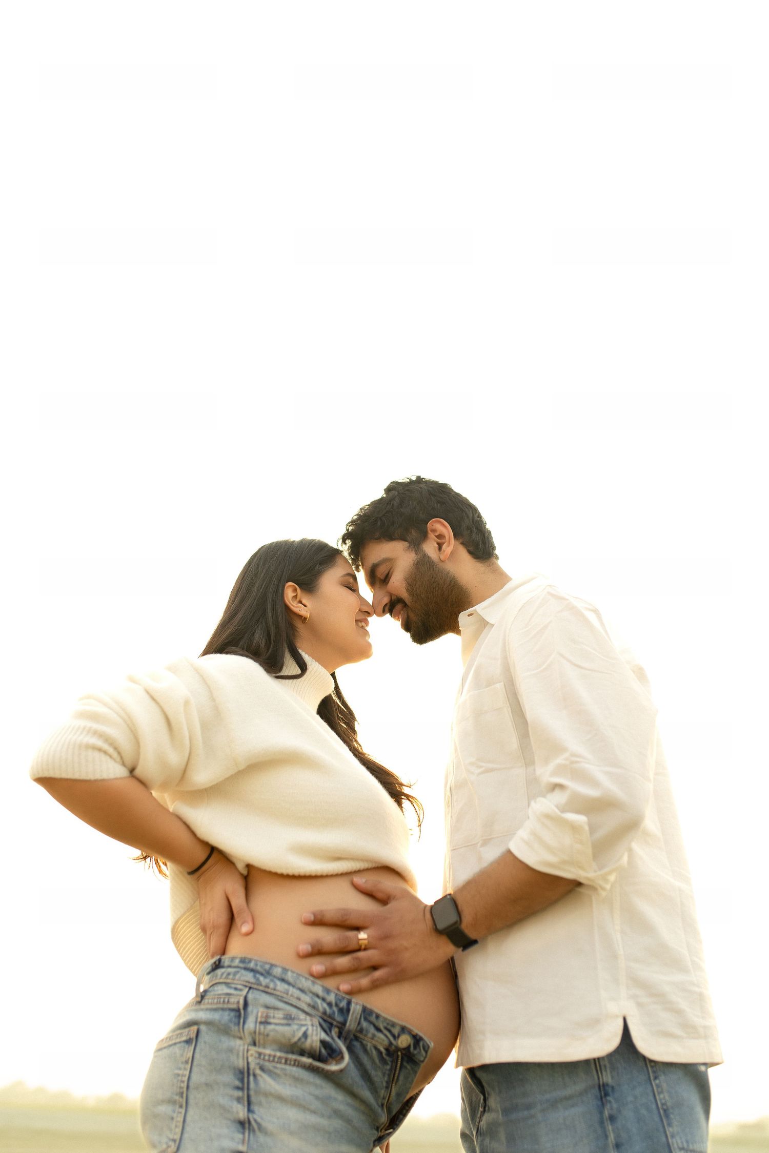 Couple sharing tender moment, man holding pregnant woman's belly outdoors in soft natural light.