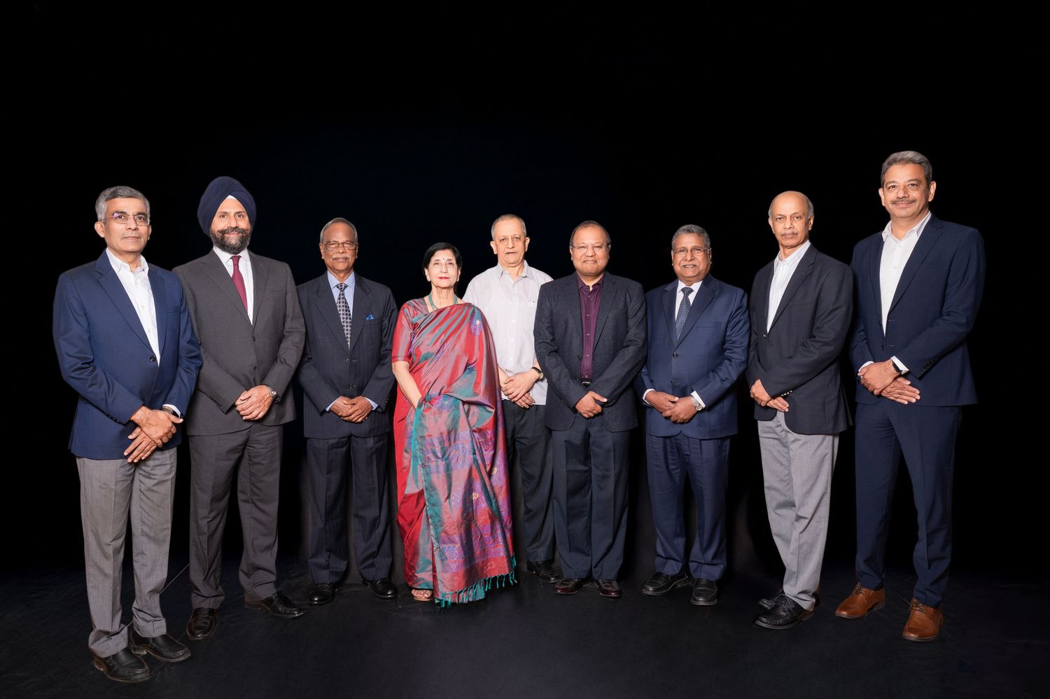 Group of nine business professionals posing together for a formal photo against a dark background.