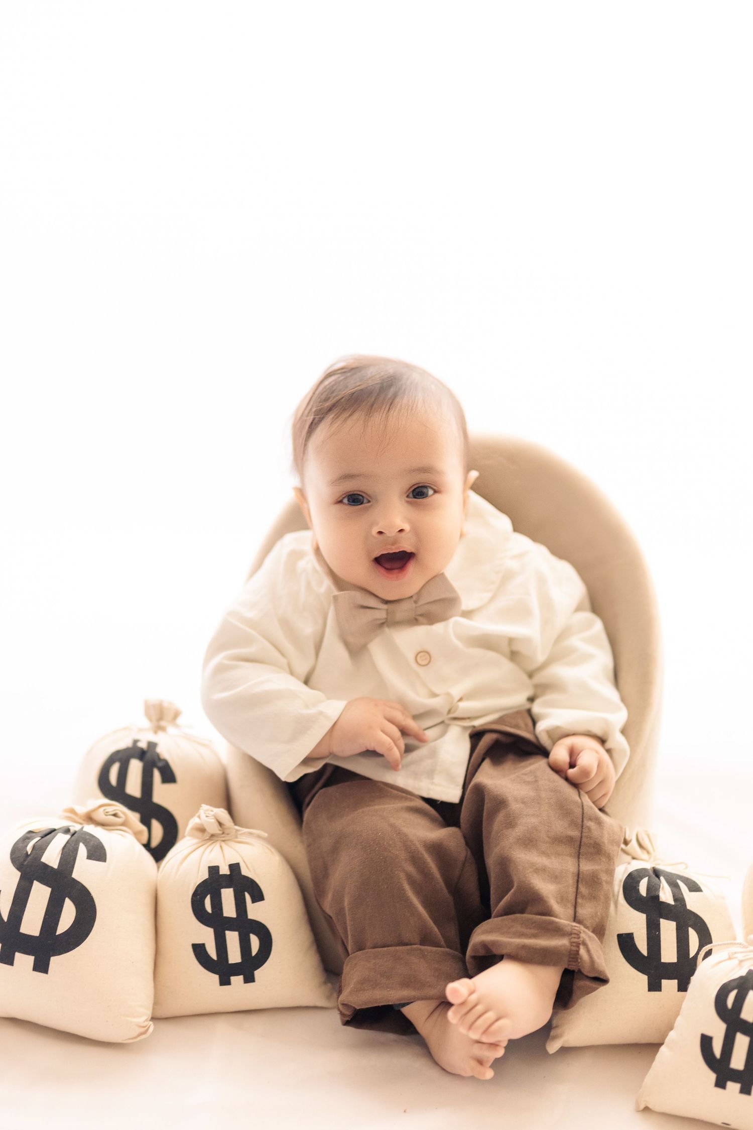 A baby in brown and white clothing sits among dollar signs in a creative financial concept photo series.