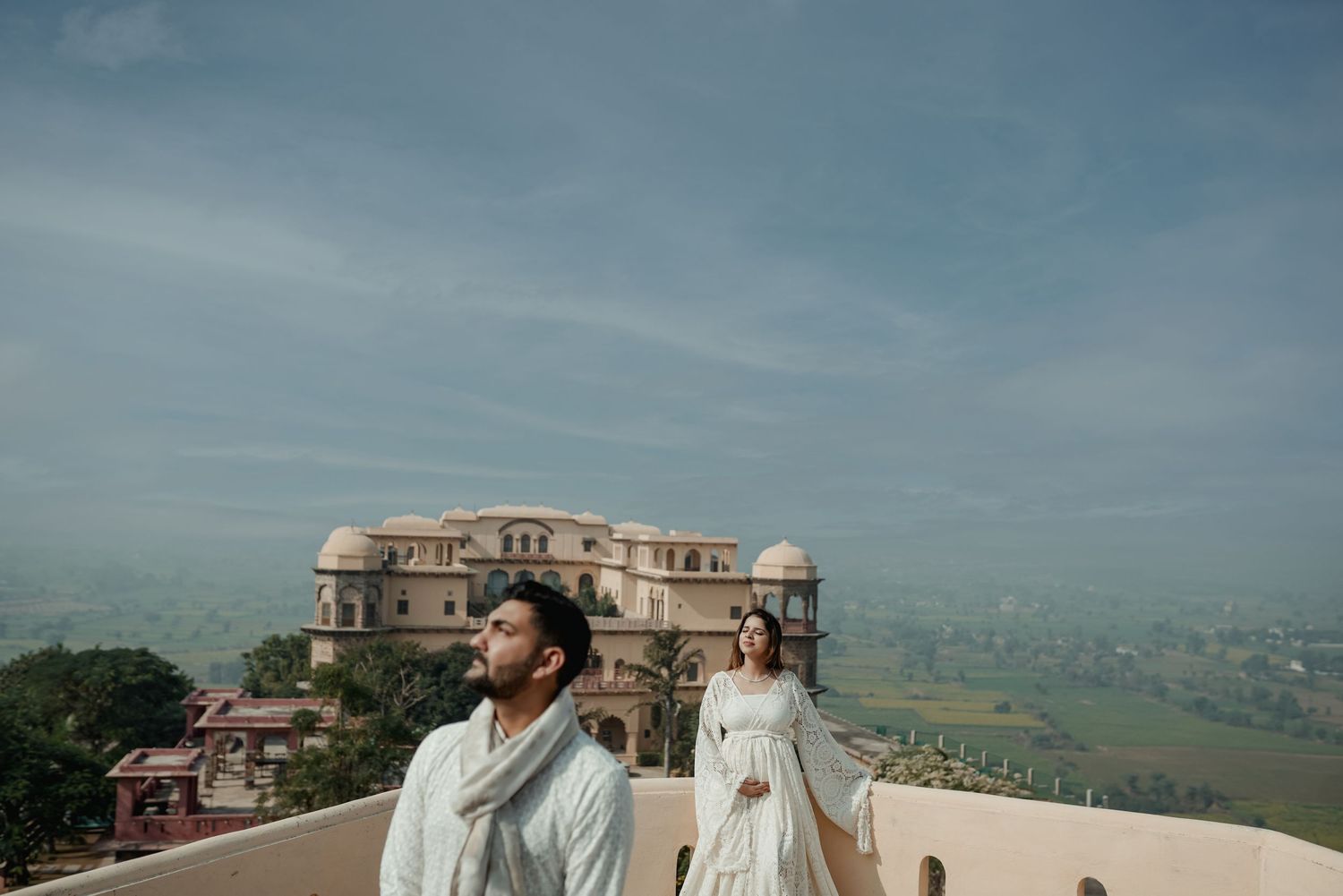 Pre-wedding photoshoot at historic palace with scenic mountain backdrop and blue sky.