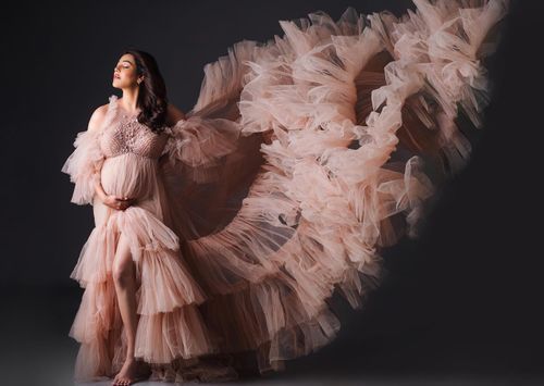 Dramatic maternity photos featuring a flowing blush tulle gown against a dark background.