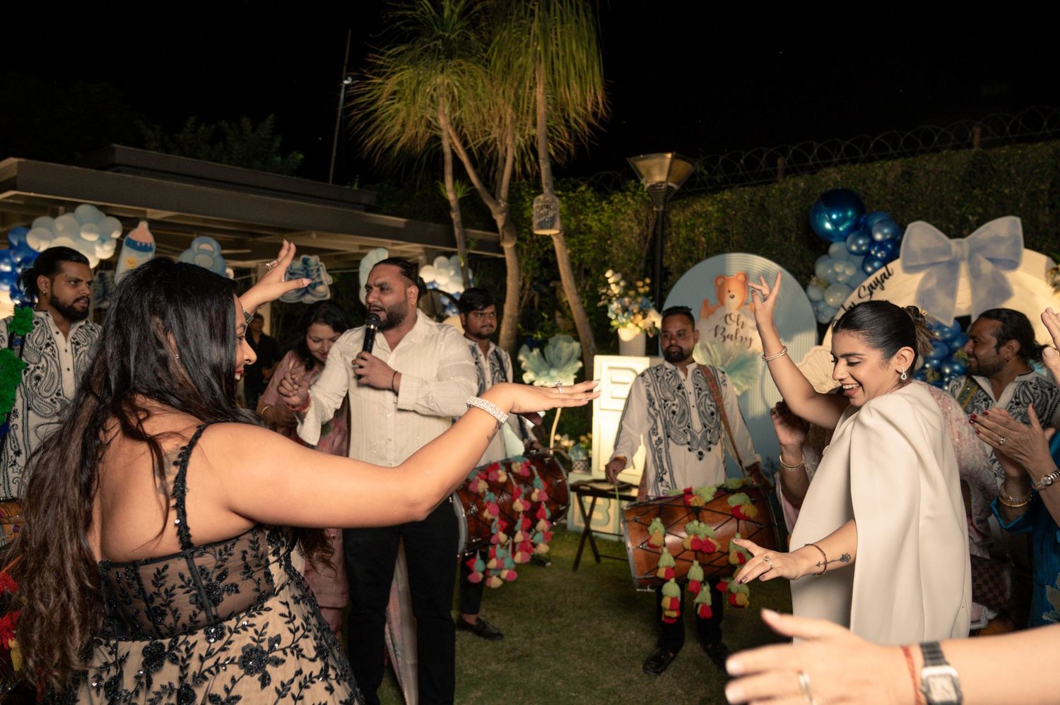 Guests dancing and celebrating at an outdoor night party with balloons and decorations in the background.