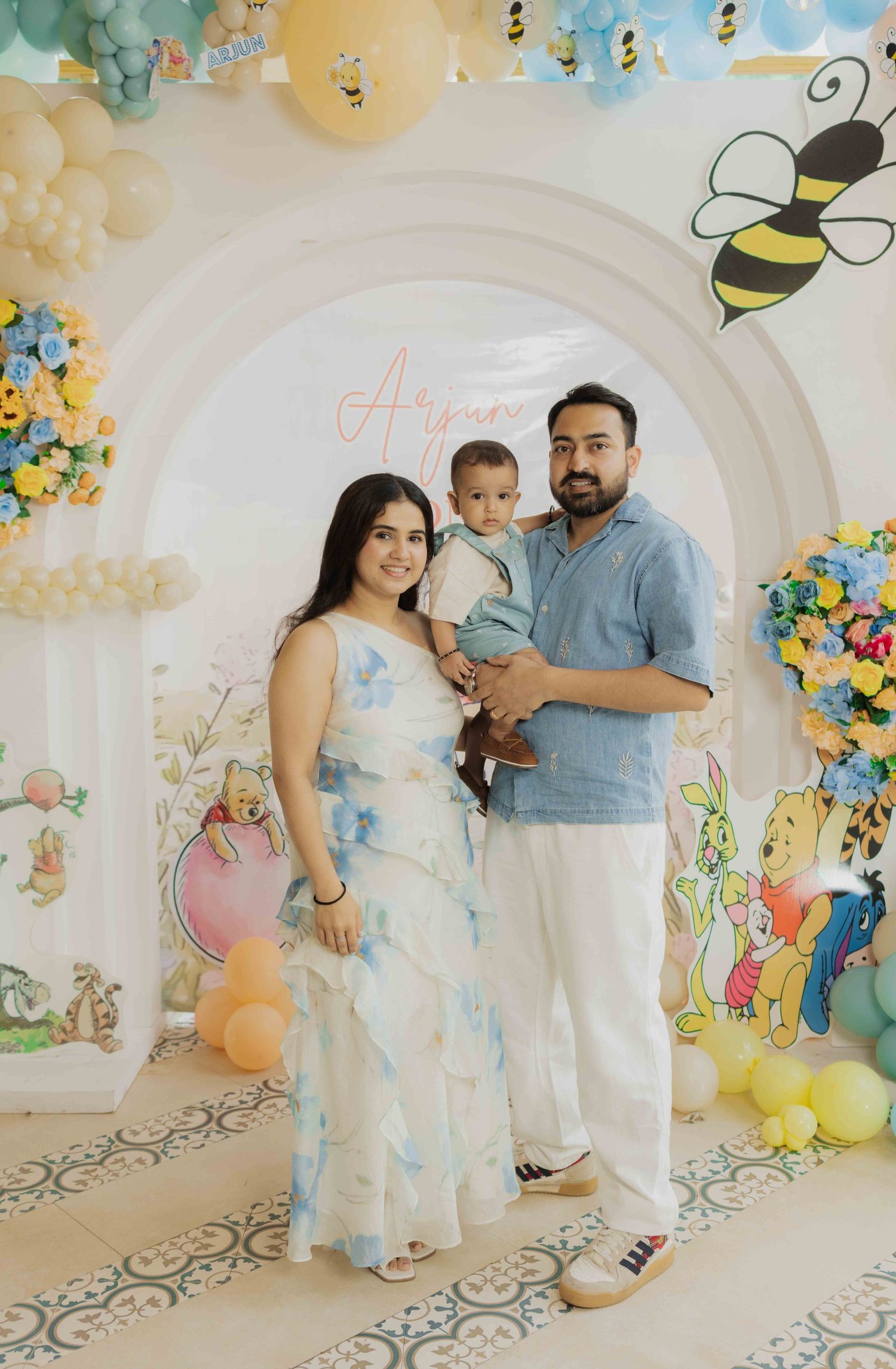 Family posing at a Winnie the Pooh themed first birthday party with balloon decorations and floral arrangements.