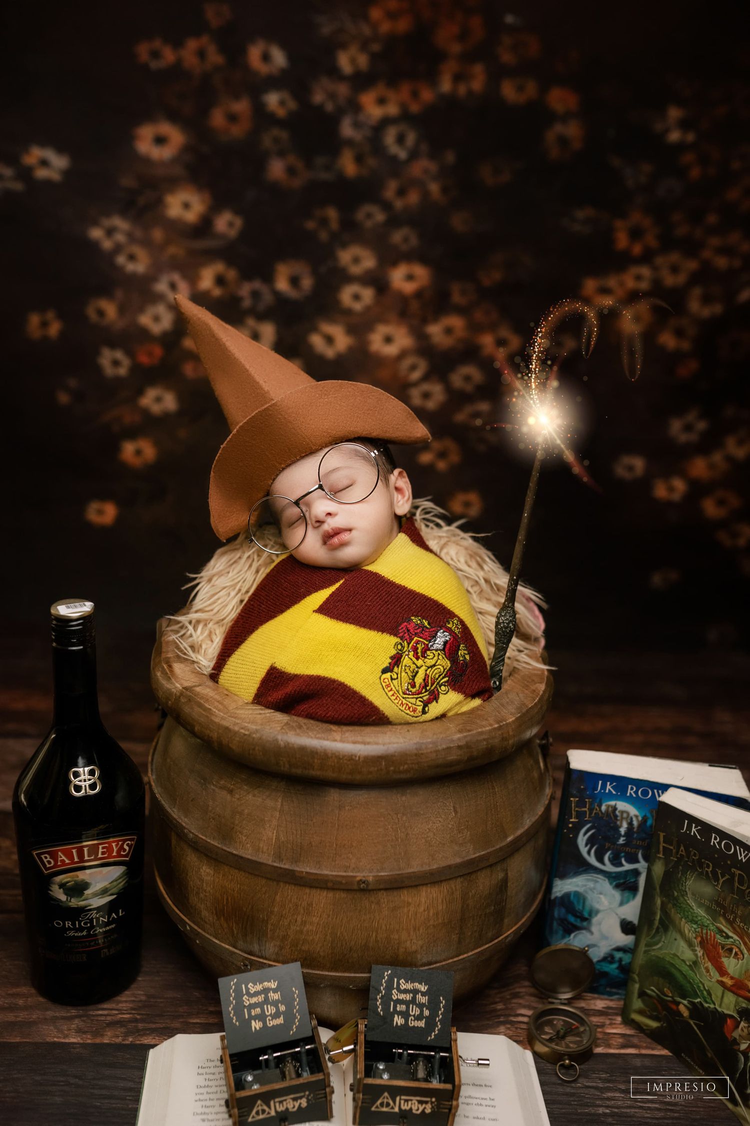 Newborn baby dressed as Harry Potter in a wooden barrel with Baileys bottle and JK Rowling books.