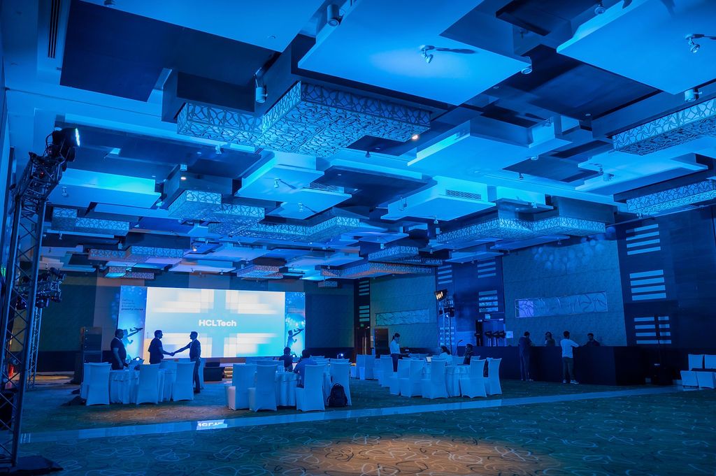 Elegant corporate event venue with blue lighting, large projection screen, and banquet tables in a modern ballroom.
