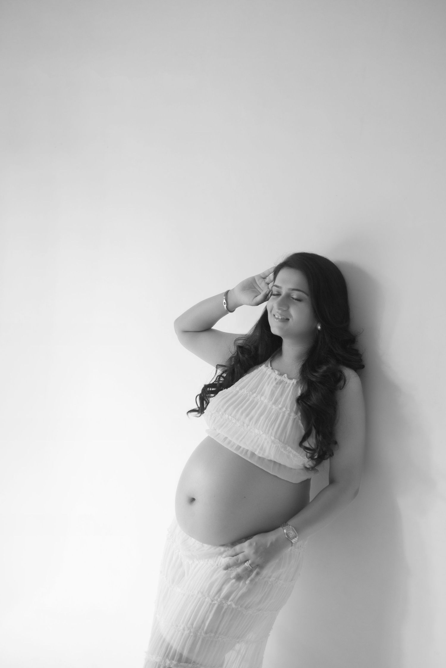 Artistic black and white maternity photo series showing a pregnant woman in white dress against a light background.