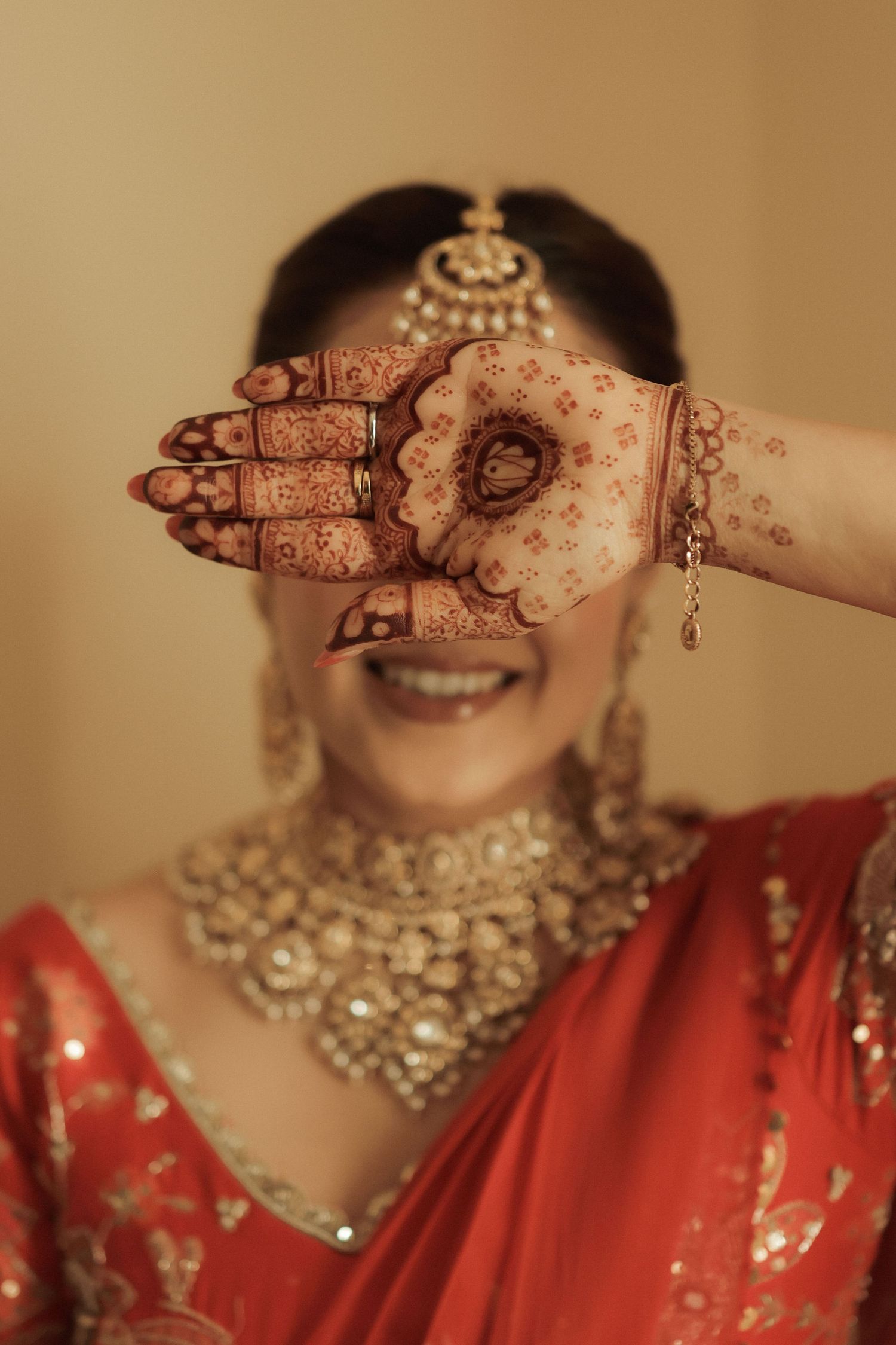 Indian bride in red saree showcasing intricate mehndi henna hand design, wearing gold jewelry and maang tikka.