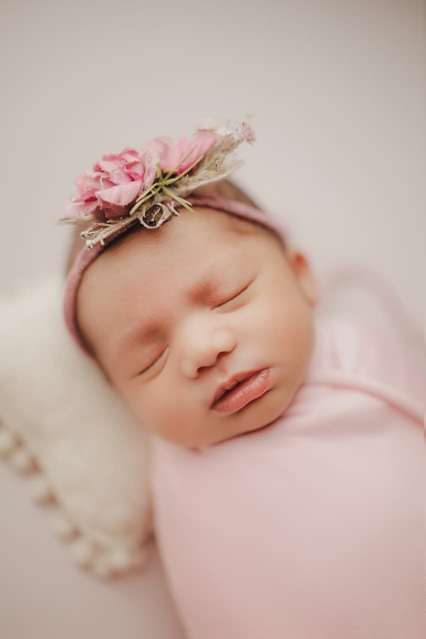 Sleeping newborn baby girl wrapped in pink swaddle wearing a delicate floral headband with pink roses.