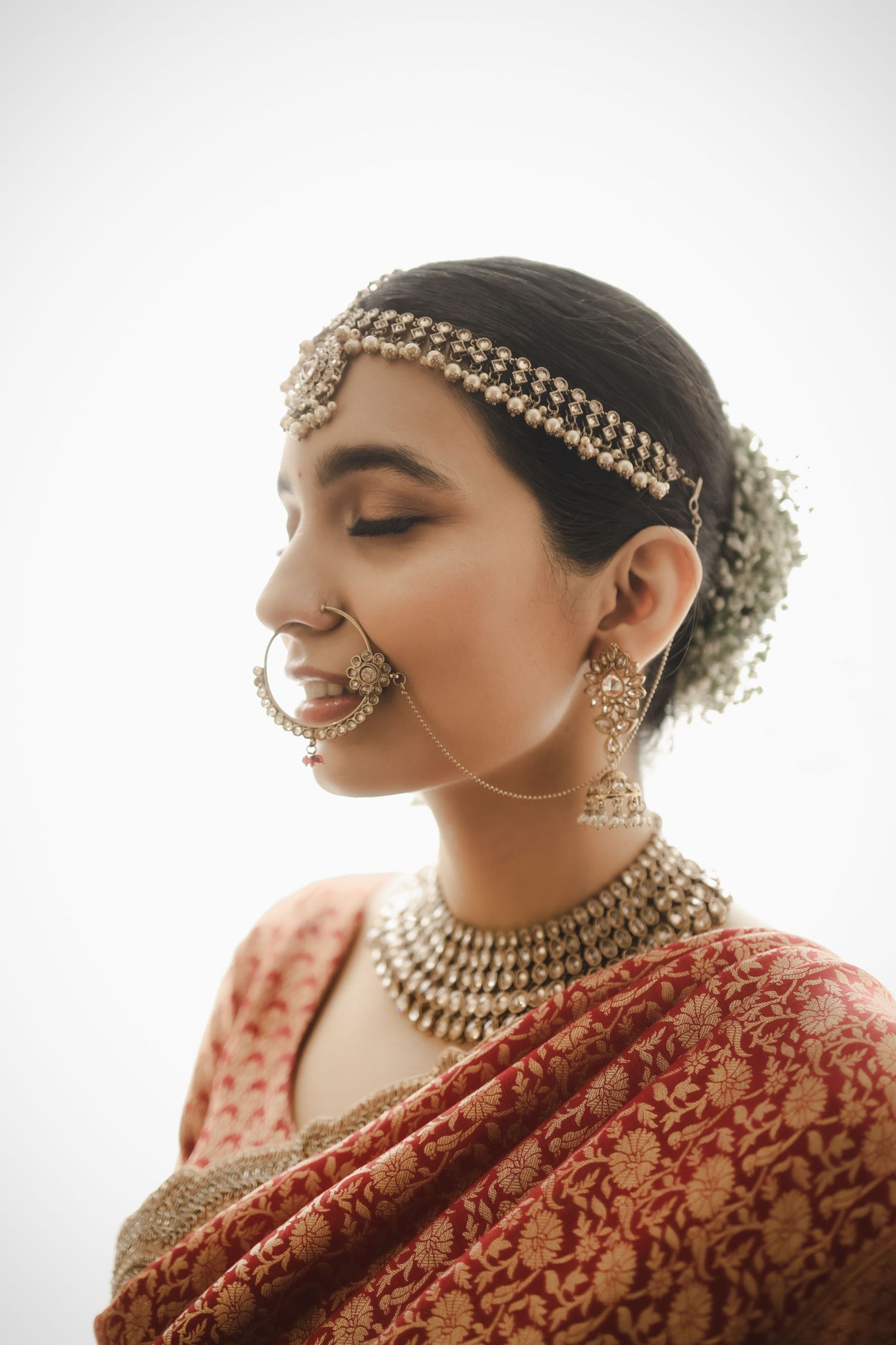 A bride wearing traditional Indian bridal attire with ornate gold jewelry and a red embroidered sari.