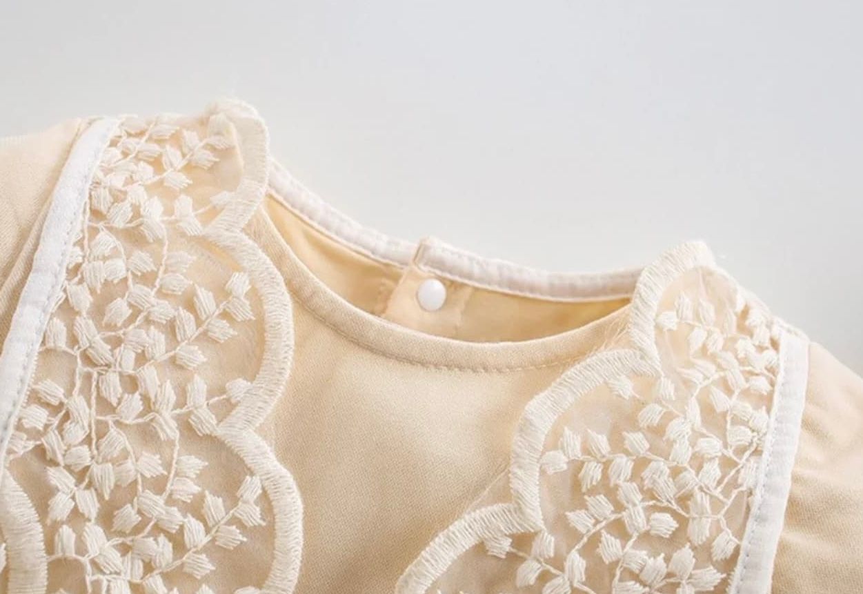 Close-up details of delicate white lace and embroidery trim on light beige fabric.