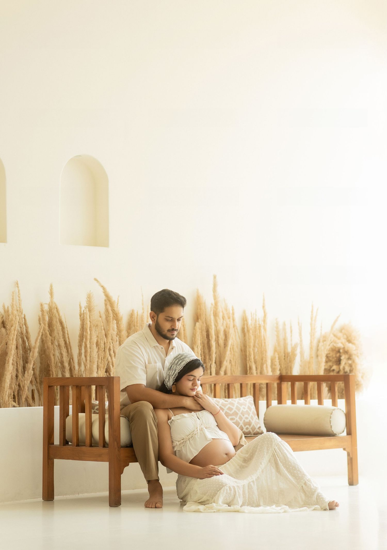 Serene maternity photo sequence showing couple in white against soft wheat backdrop in natural light studio setting.