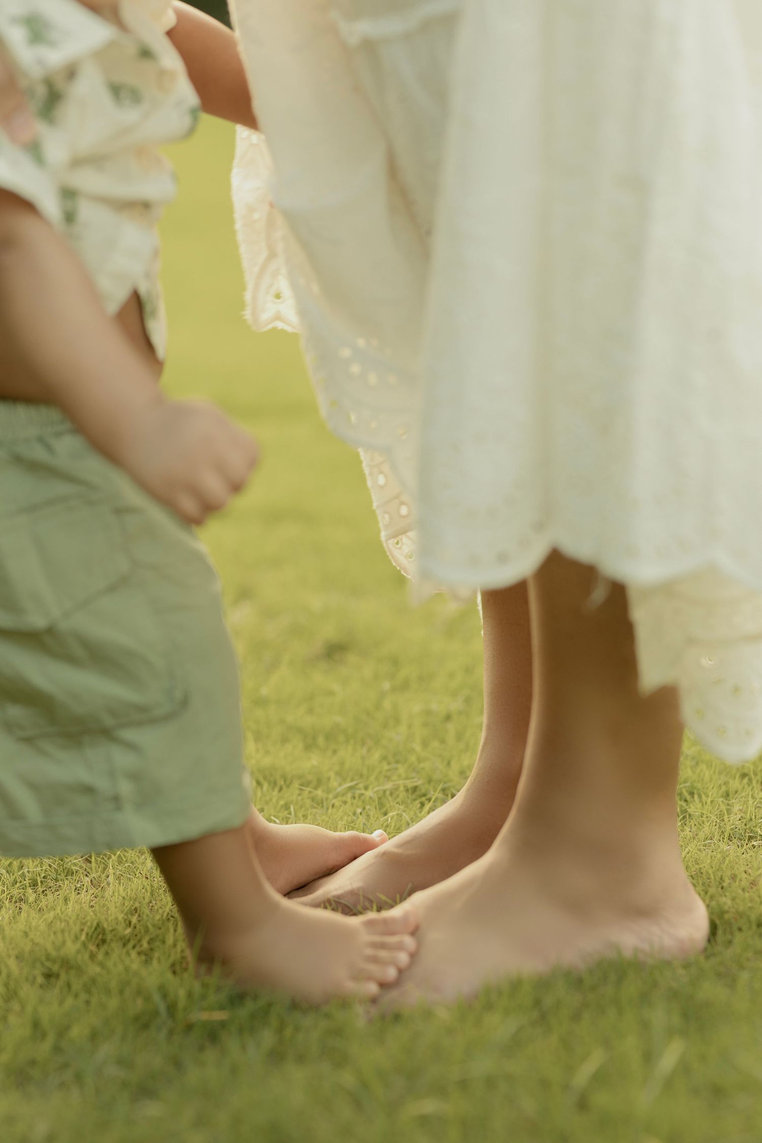 Bare feet of multiple people standing on lush green grass, with someone wearing a white flowing dress.