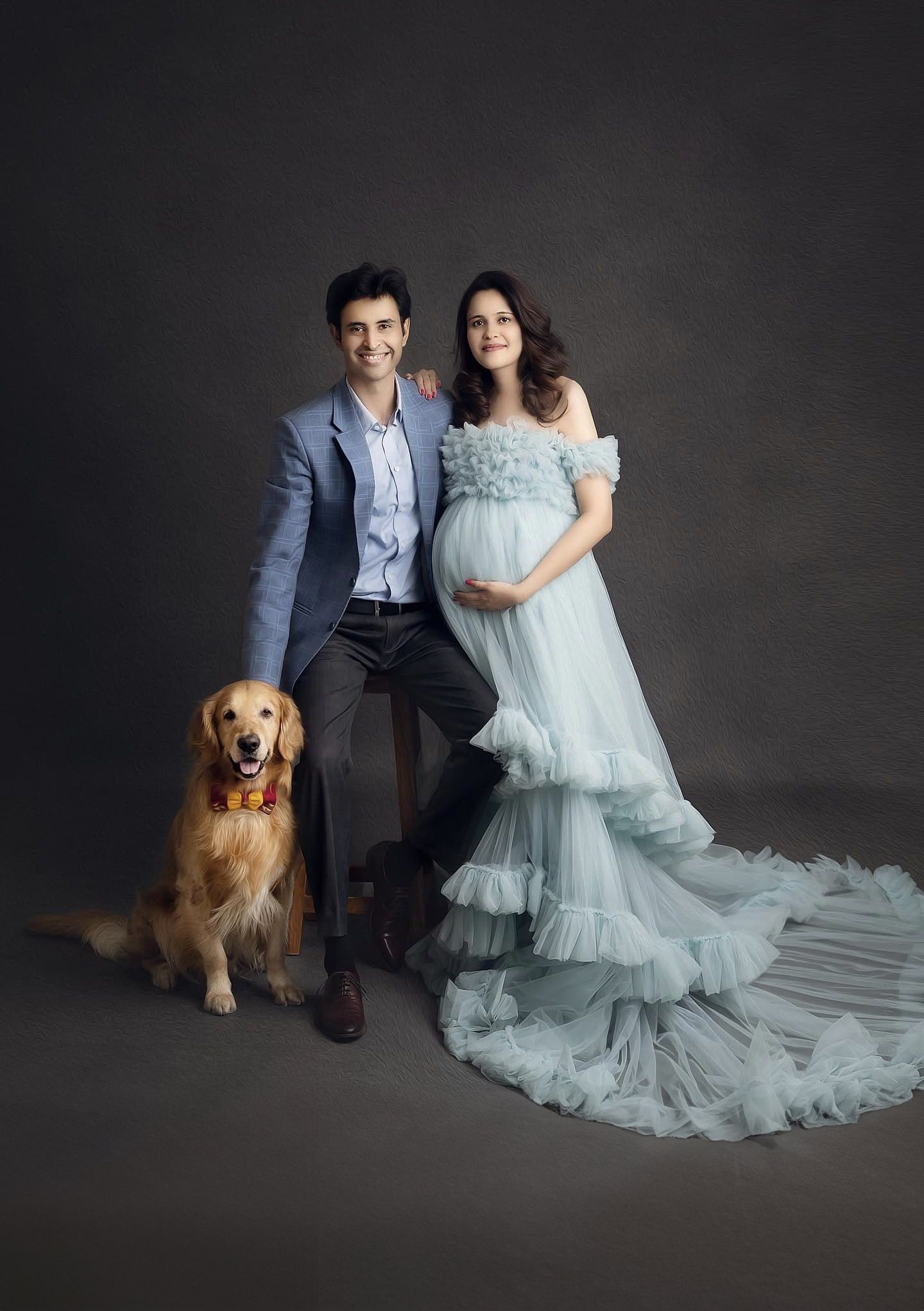 Maternity photoshoot featuring a couple and their golden retriever against a dark backdrop.