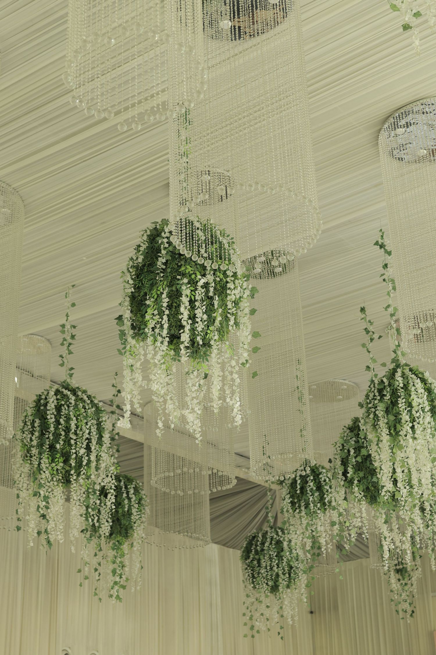 Elegant hanging floral arrangements with white wisteria and green ivy cascading from decorative ceiling fixtures.