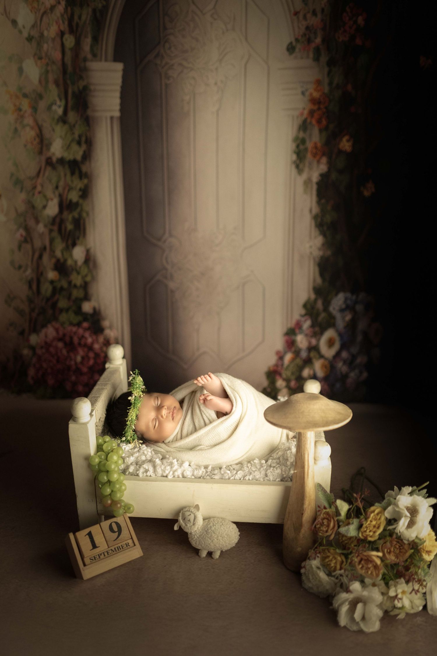 Newborn baby swaddled in white wrap sleeping in a tiny bed with floral backdrop and September 19 date block.