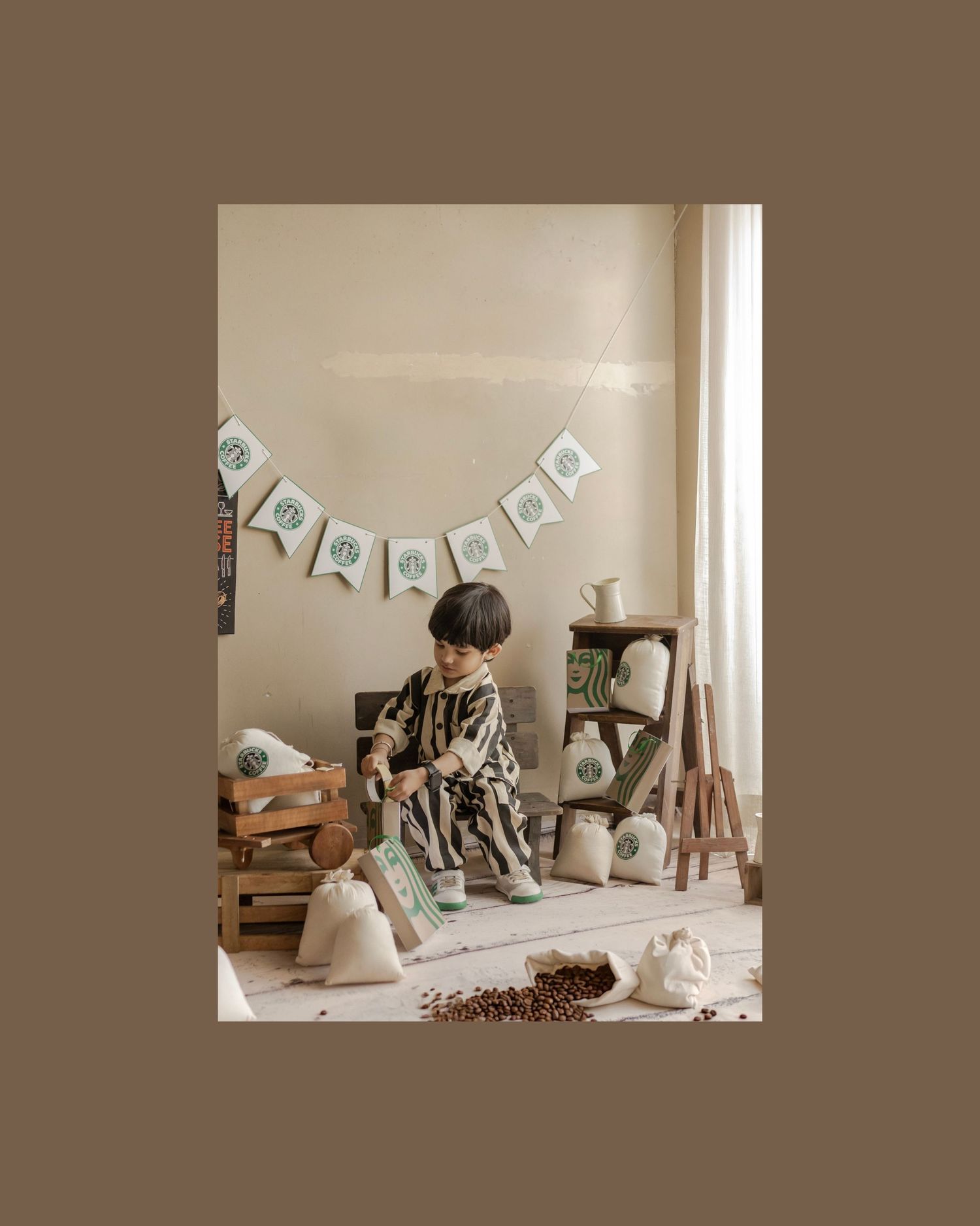 Young child in patterned outfit sits on floor surrounded by rustic wooden props and burlap sacks in cozy styled photo.