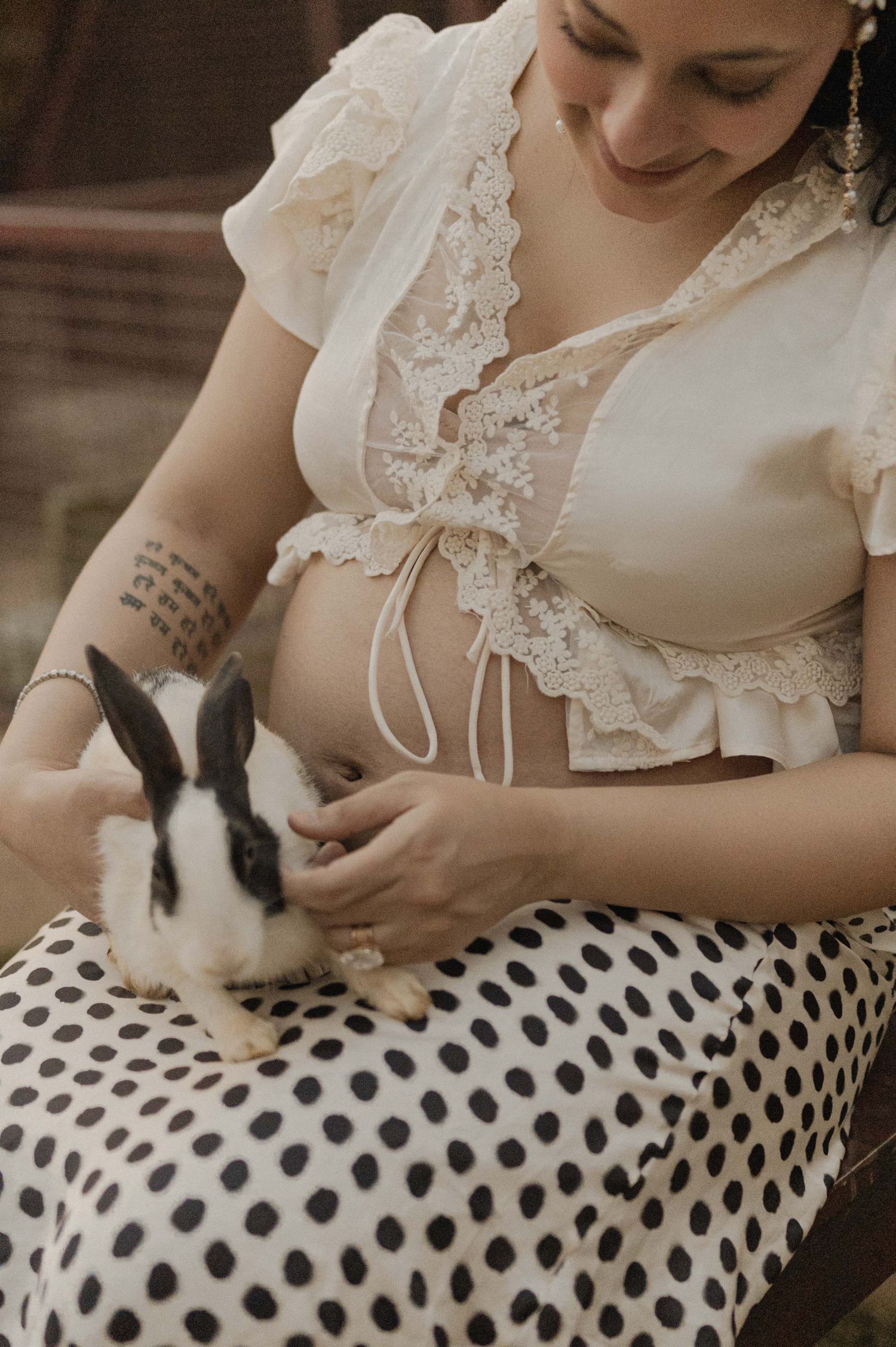 Pregnant woman in lace crop top holding a black and white rabbit on her polka dot skirt.