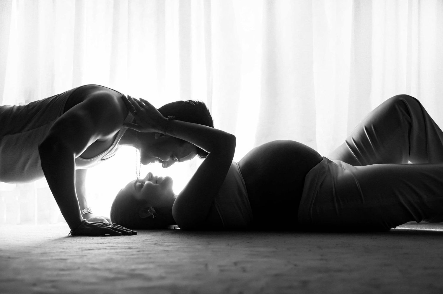 A dramatic black and white silhouette of two people resting together for maternity shoot with husband.