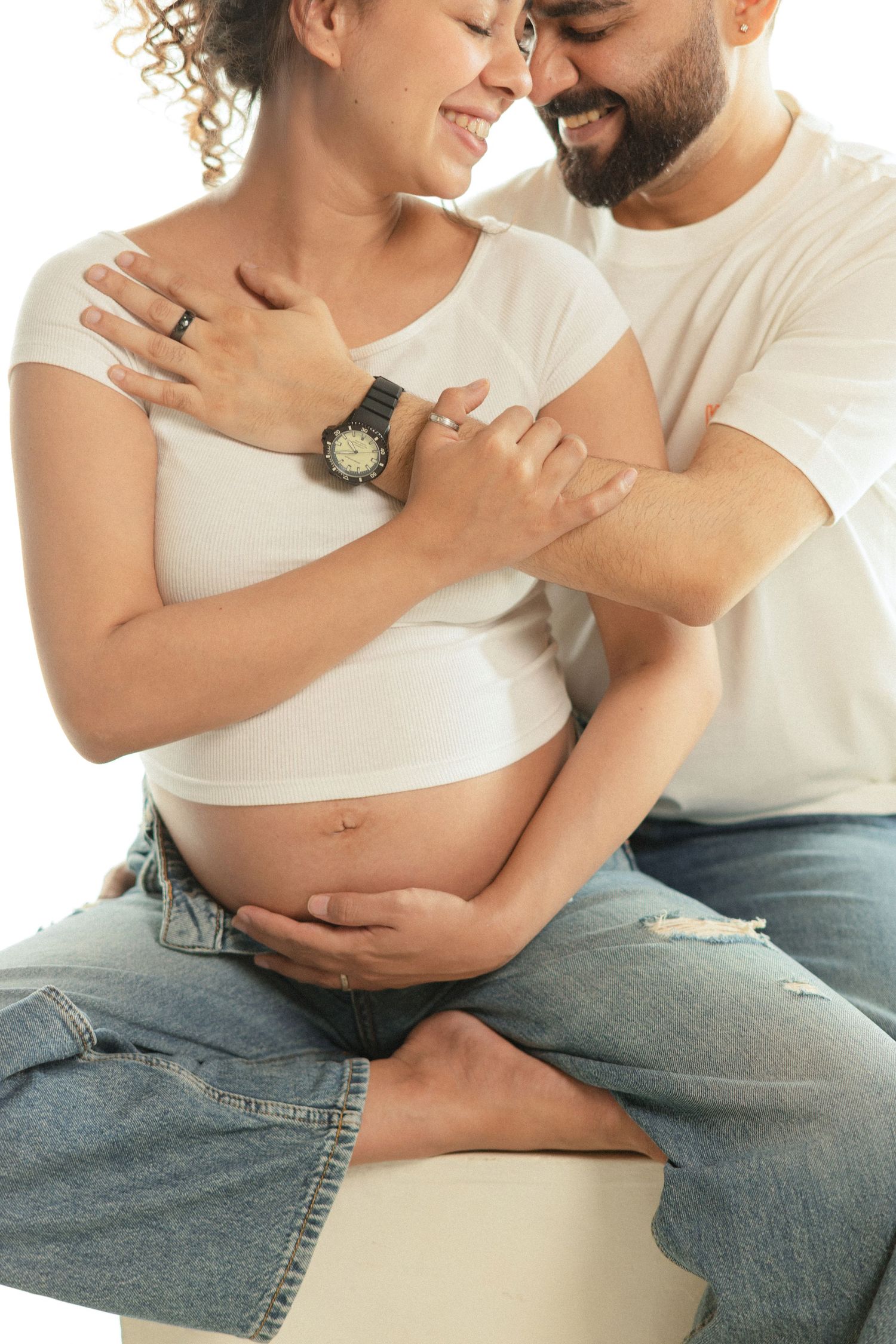 Intimate maternity photo series showing couple embracing and touching pregnant belly while sitting on bed in casual clothing.