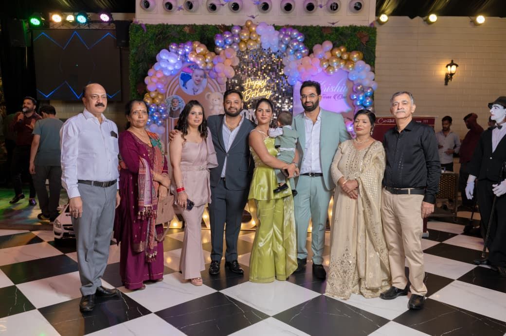 Group of elegantly dressed people posing together at a festive celebration with balloon decorations.