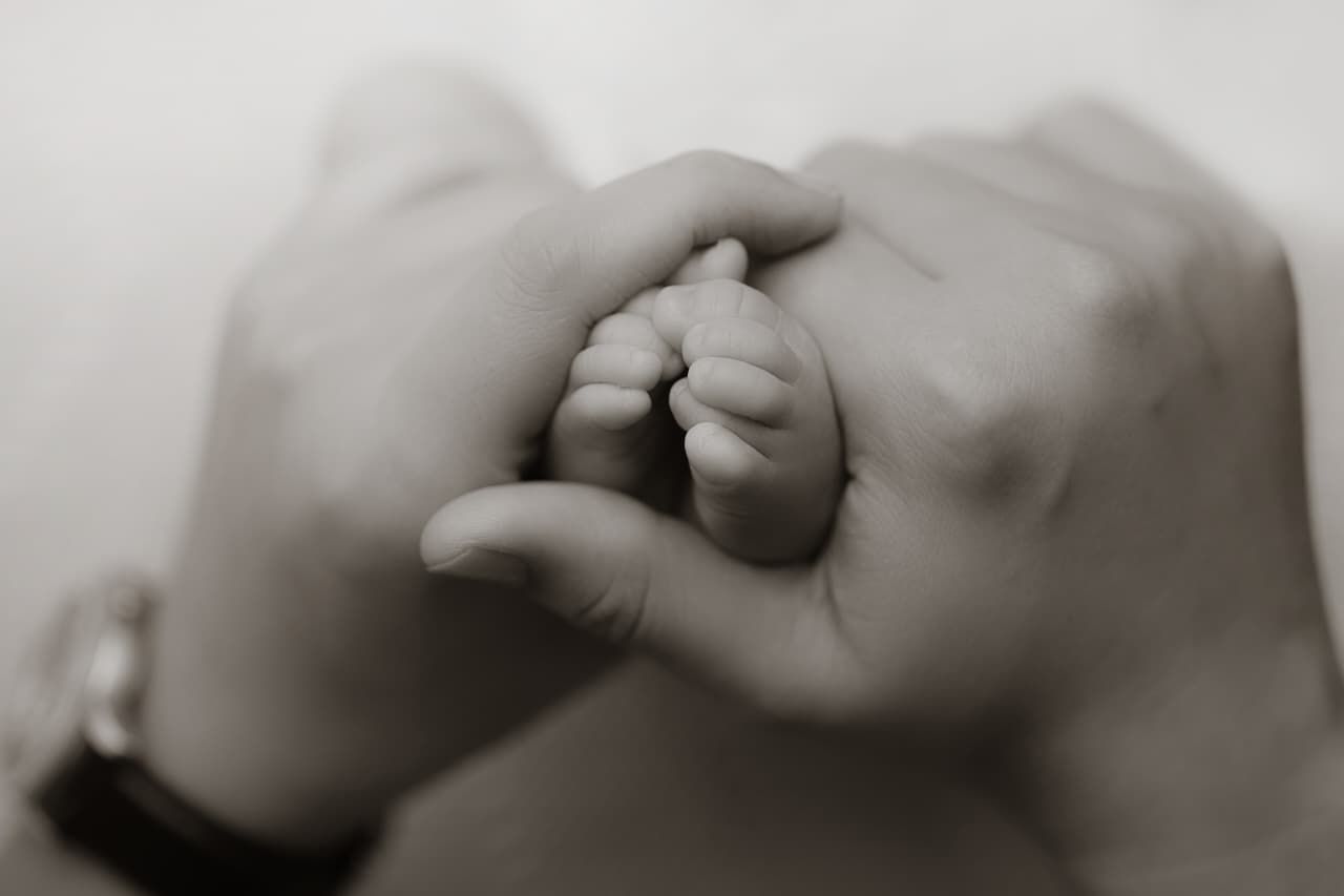 Black and white photo of adult hands gently cradling a tiny newborn baby foot.