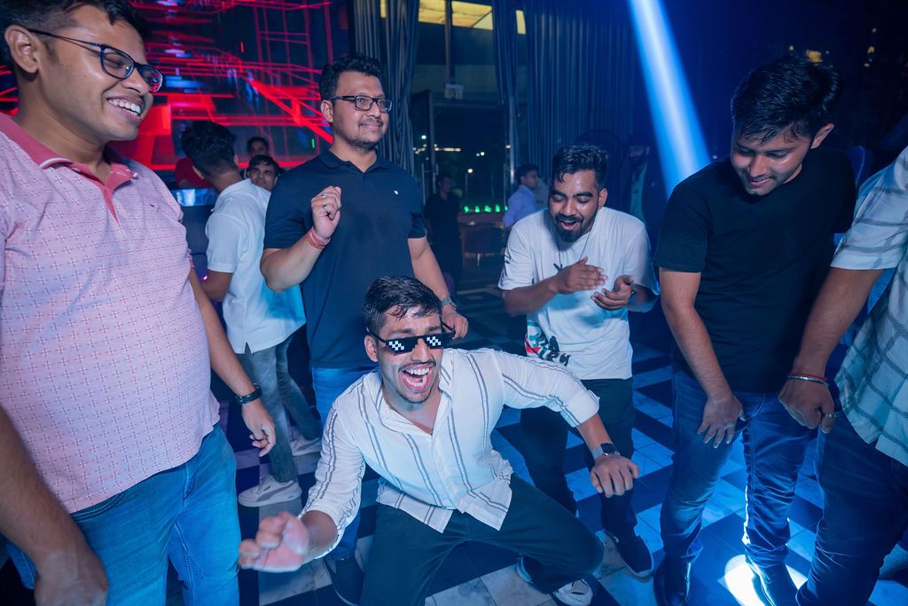 Group of young men dancing and celebrating at a nightclub with blue laser lights.