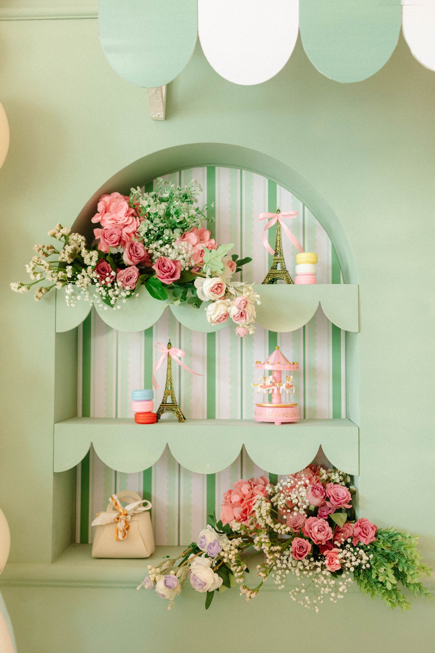 Mint green decorative shelf with pink roses, Eiffel Tower figurine, carousel, and macarons in a whimsical pastel display.