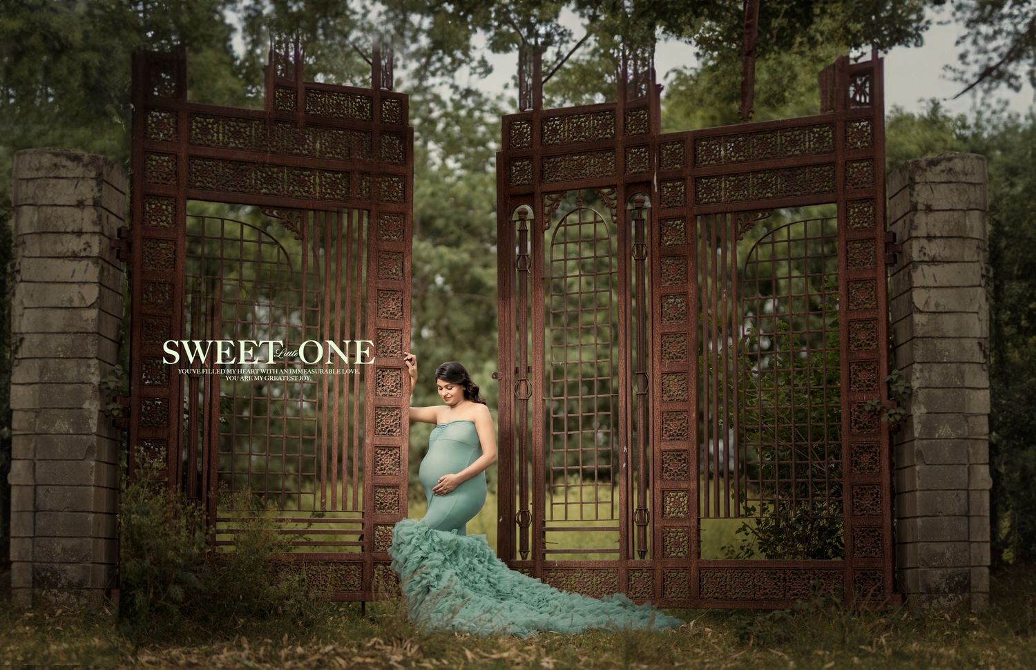 A dreamy maternity portrait at an ornate iron gate entrance amid lush greenery.