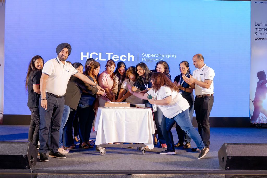 A series of people in white shirts working at tables during what appears to be a tech conference or event.