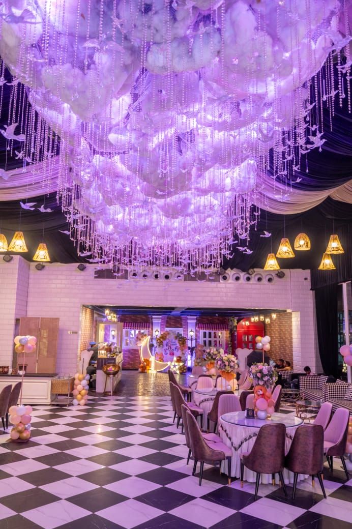 Elegant event hall with purple LED chandelier, black and white checkered floor, and decorated tables with floral centerpieces.