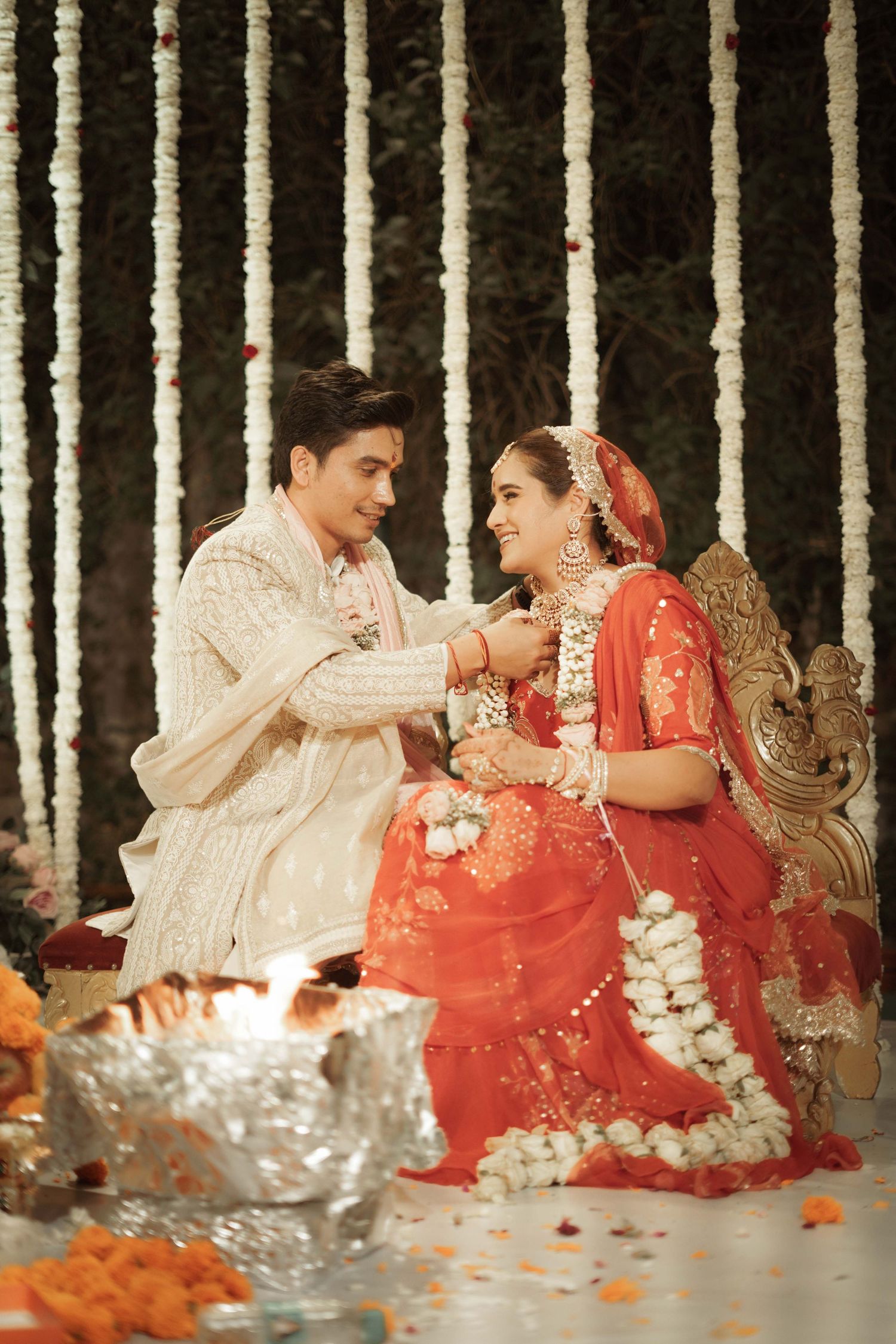 Indian bride in red lehenga and groom in white sherwani perform traditional Hindu wedding ceremony by sacred fire.