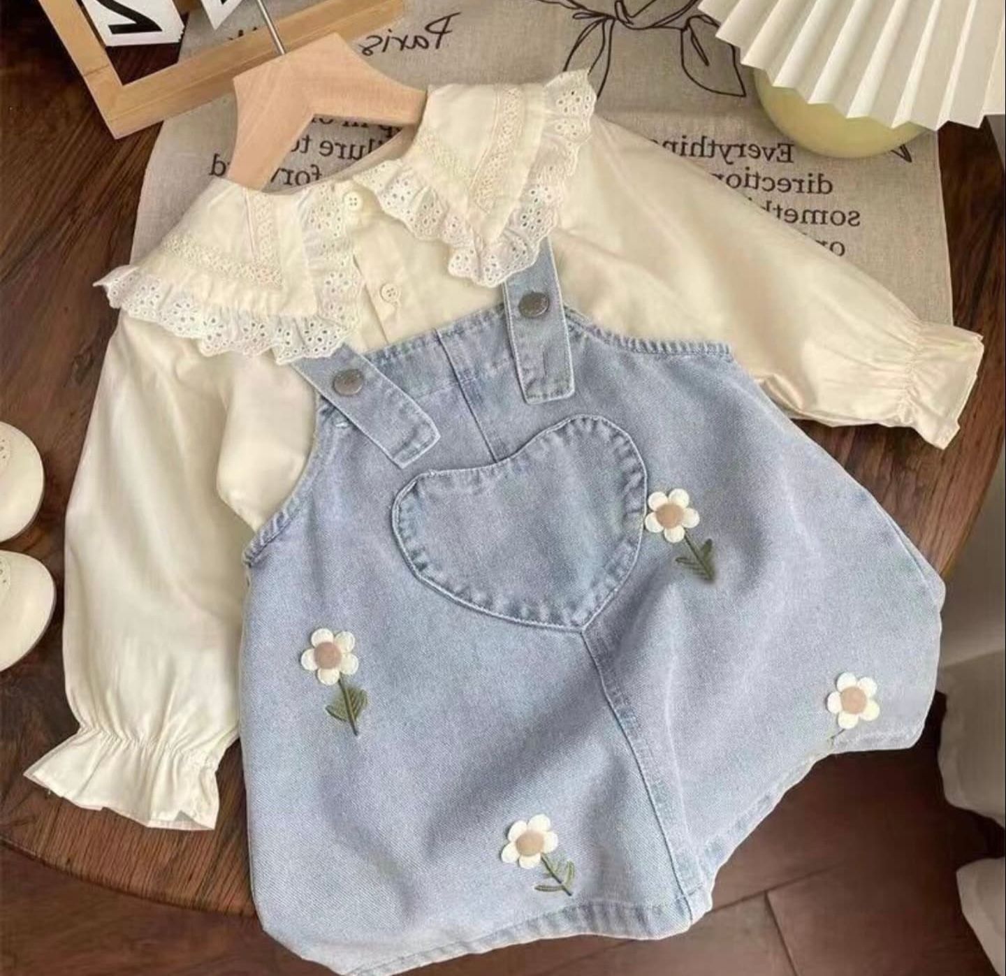 Light blue denim skirt with white lace trim and daisy flower appliques laid flat on wooden surface.