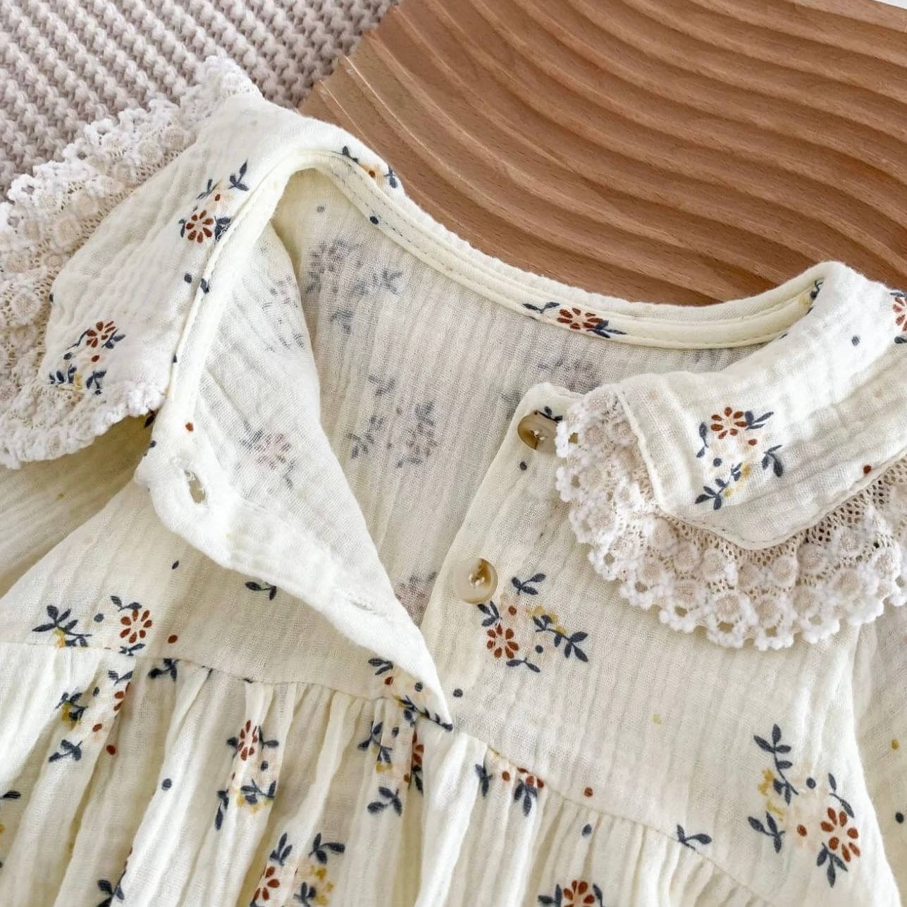 Series of white cotton dresses with delicate floral embroidery and pintuck details hanging in a row.