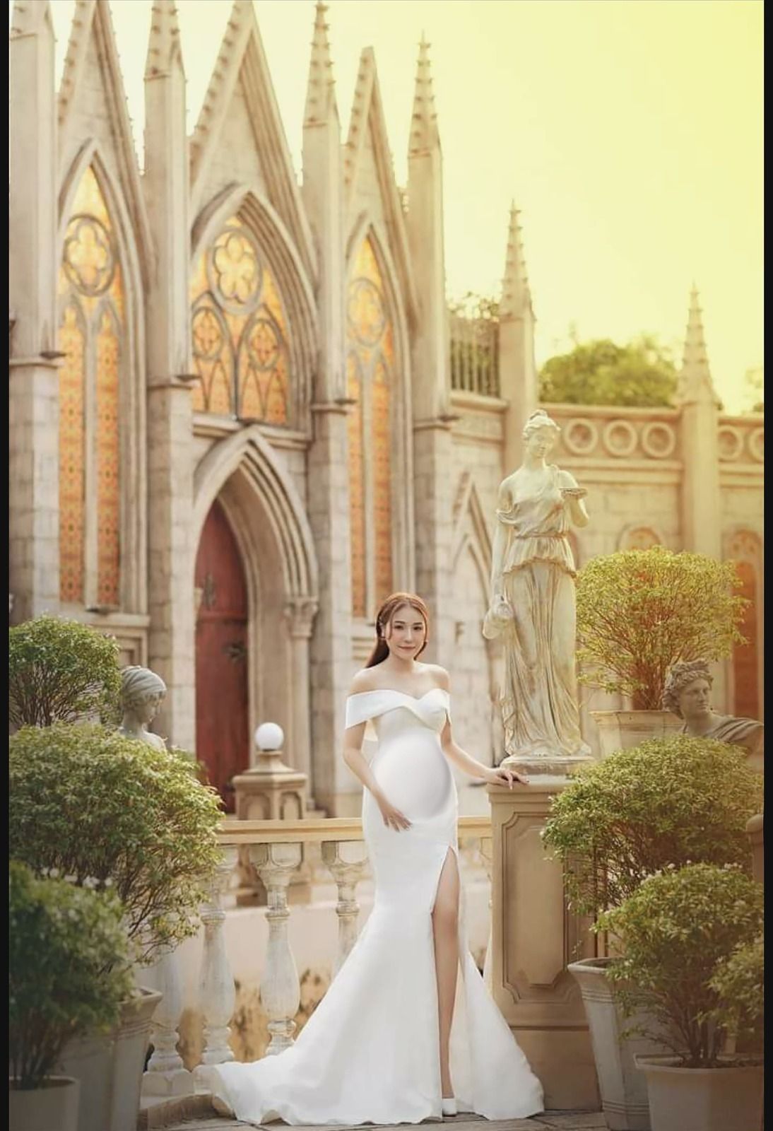 Elegant maternity portrait in white gown against Gothic cathedral architecture.