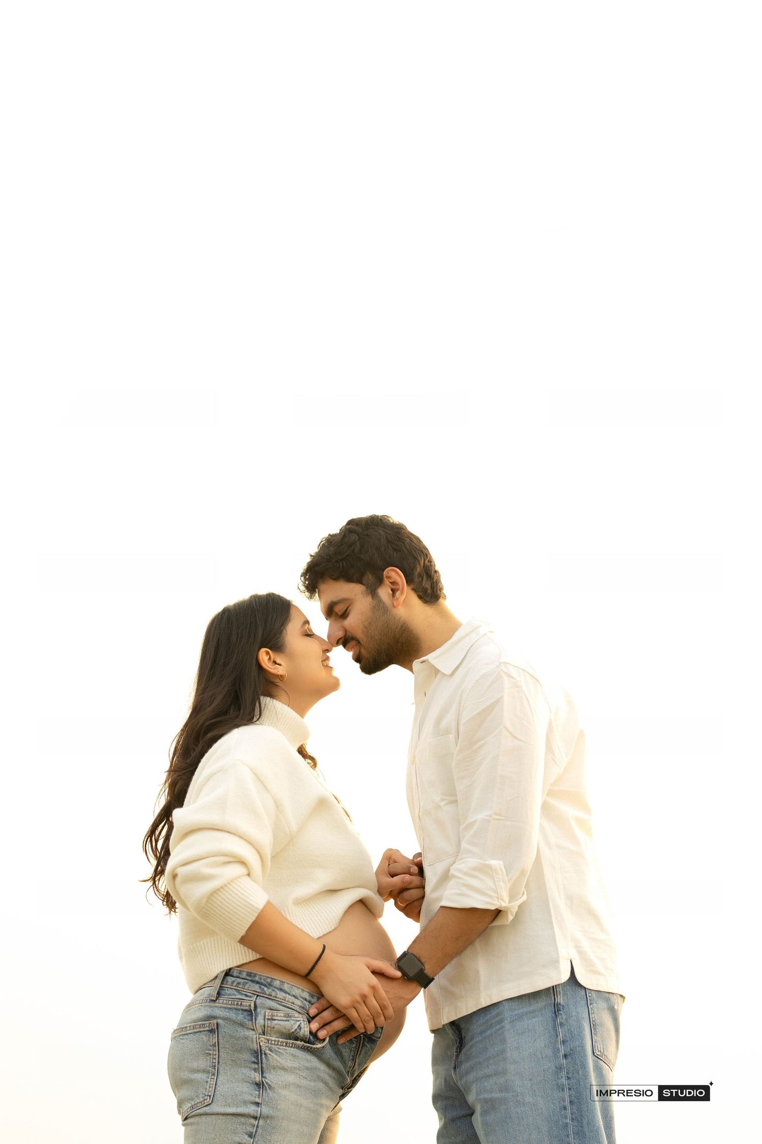 A couple shares a tender moment, nearly kissing, as the woman cradles her baby bump during a maternity photoshoot.