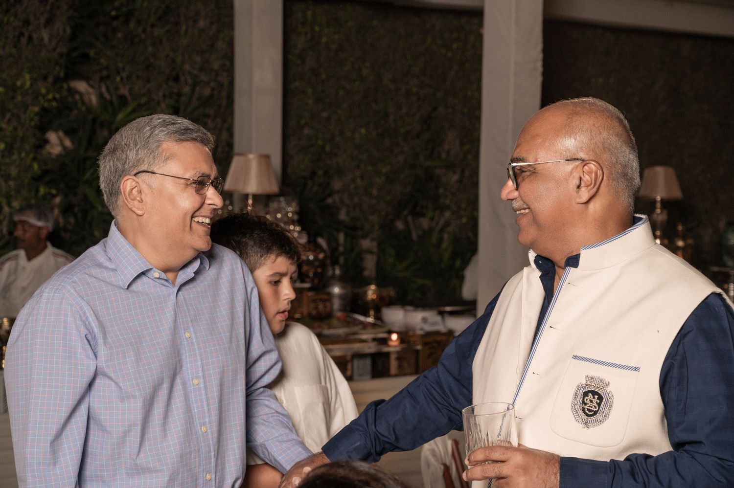 Two men in casual attire share a conversation at an evening outdoor social gathering.