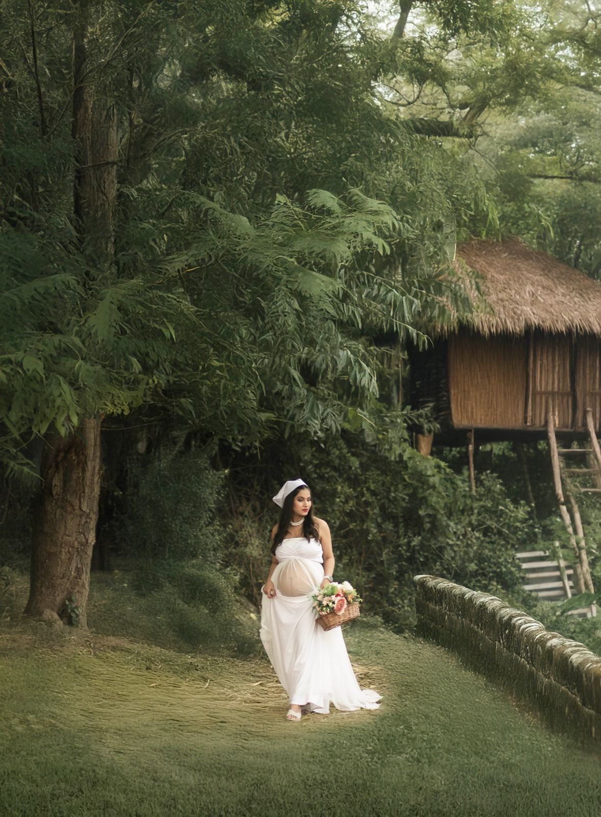 Romantic maternity portrait in white dress near a rustic treehouse surrounded by lush greenery.
