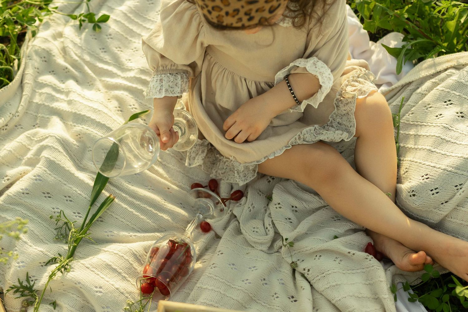 Young woman in lace dress sitting on white blanket outdoors during a peaceful garden picnic.