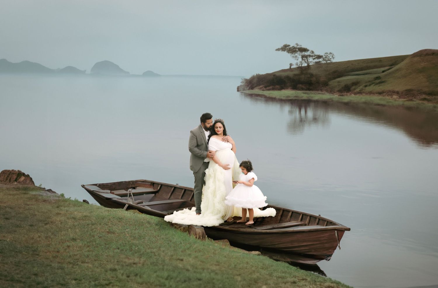 Romantic maternity photography boat scene on tranquil lake with mountain backdrop.