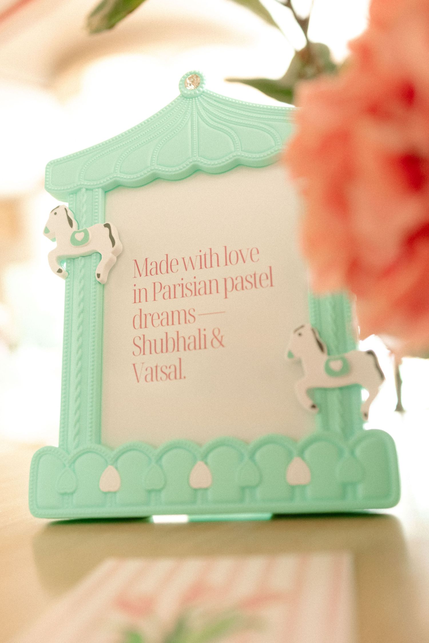 Mint green carousel-themed photo frame with horses displaying a pastel pink quote by Shubhali and Vatsal on a table.