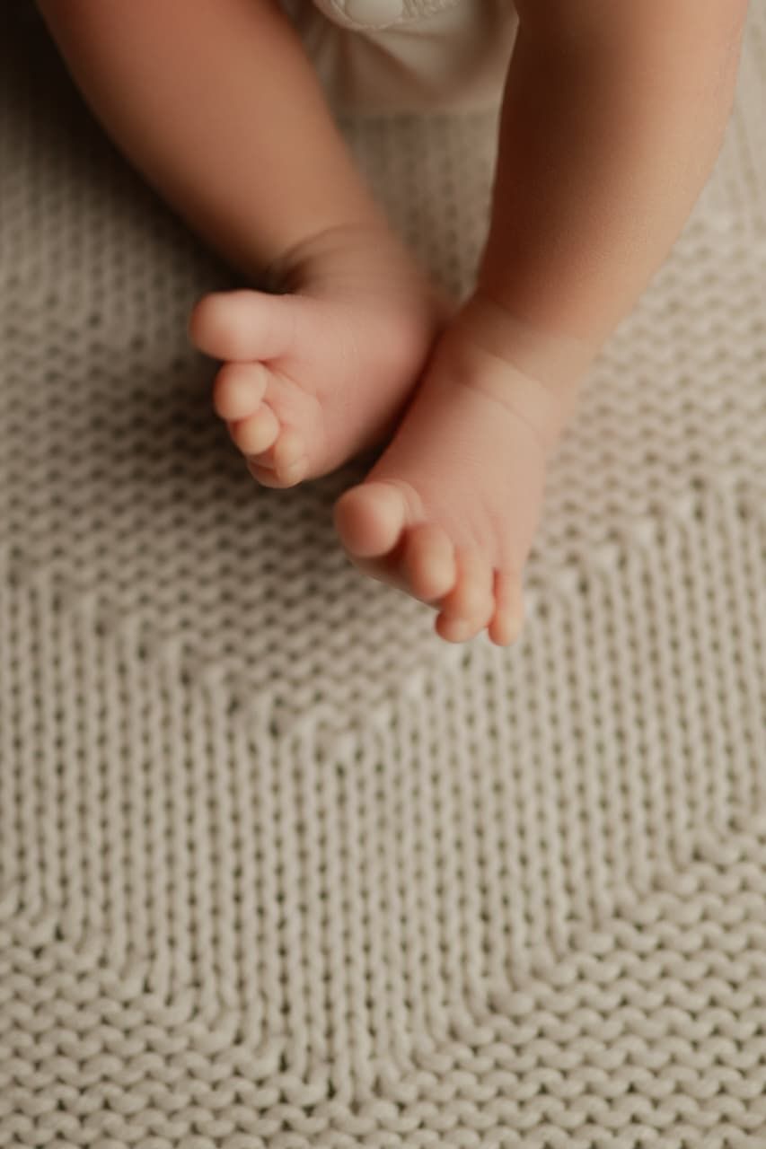Close-up of tiny newborn baby feet resting on a soft cream knit blanket.