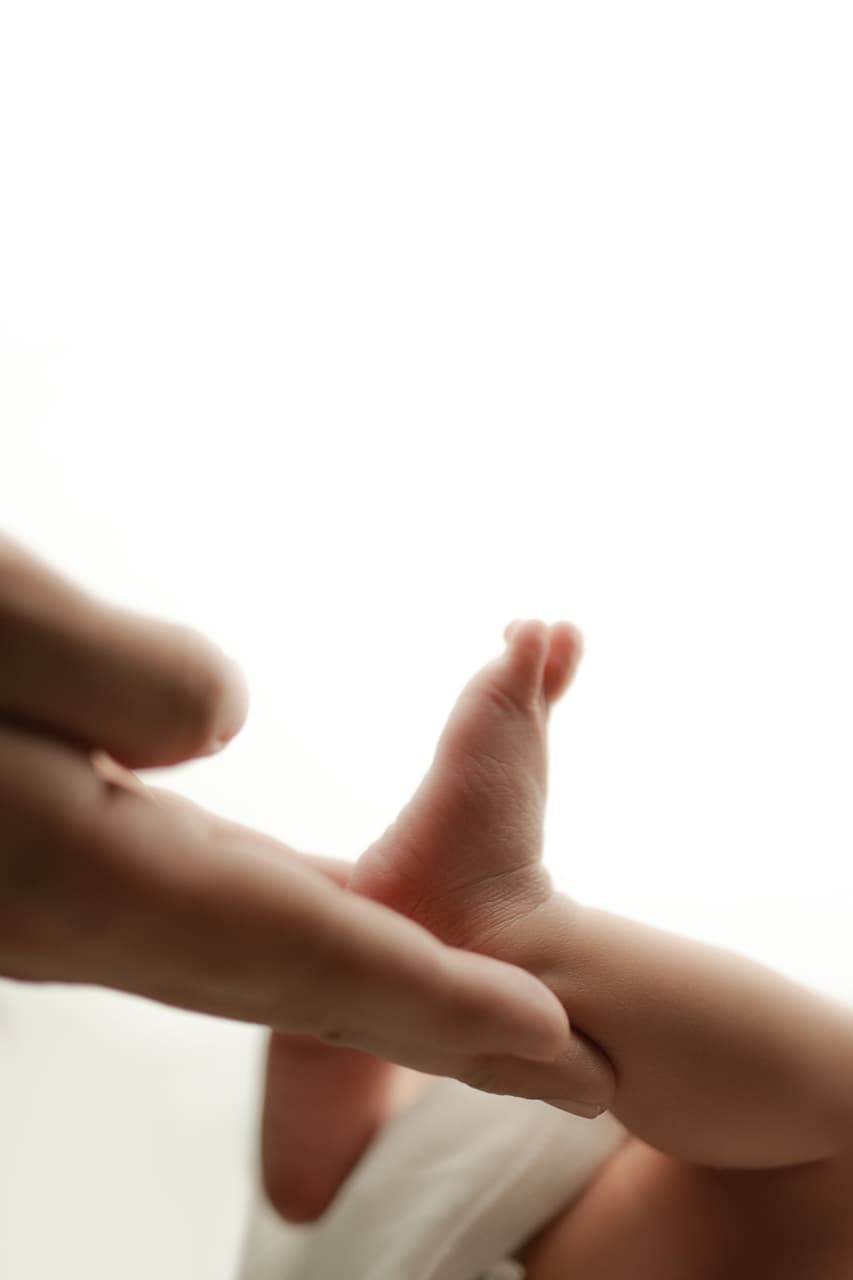 Close-up of an adult hand gently holding a tiny newborn baby foot against a white background.