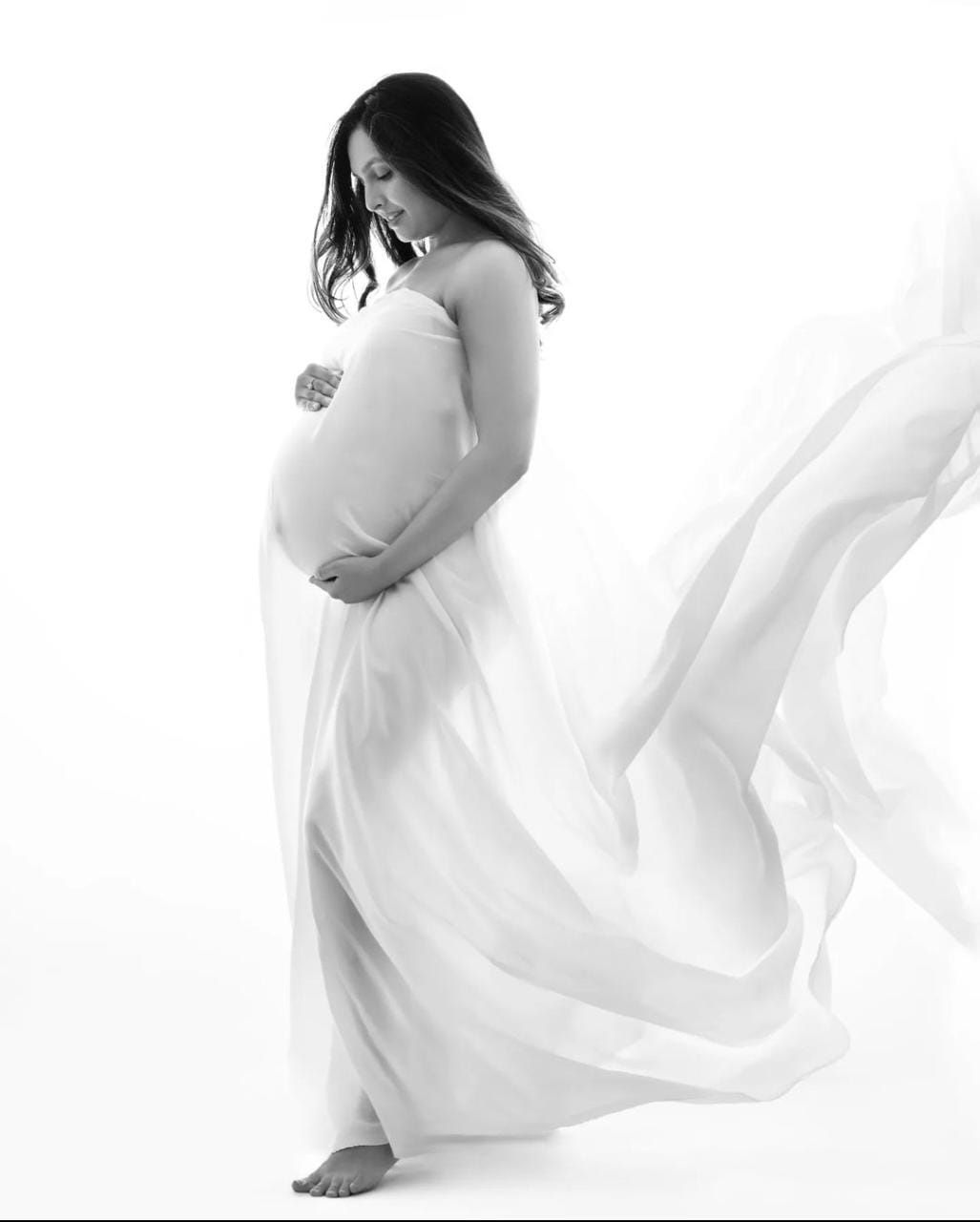 Flowing white fabric maternity portraits with ethereal movement against light background.