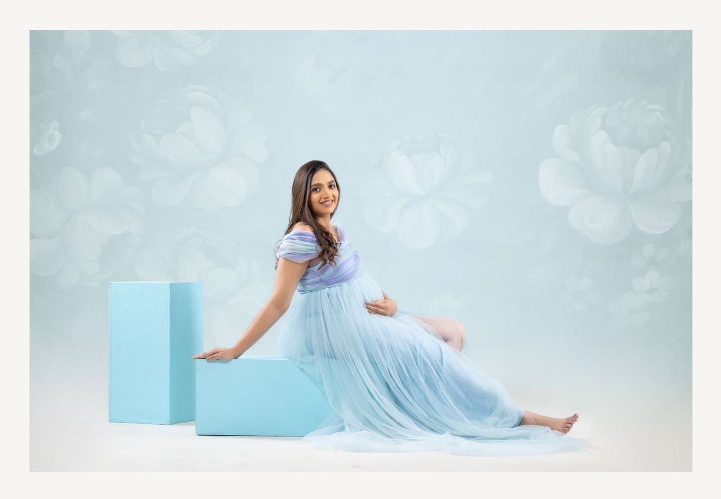 Maternity photoshoot with woman in flowing light blue dress against dreamy backdrop.